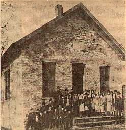 Historic photo of 1800s log cabin school with group of people in front