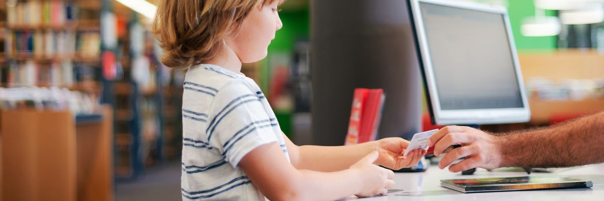 Photo of young child being handed a card by a staff member at a library desk