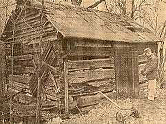 Historic black and white photo of log cabin with man standing outside