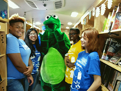 Group photo of library volunteers and library mascot in the stacks