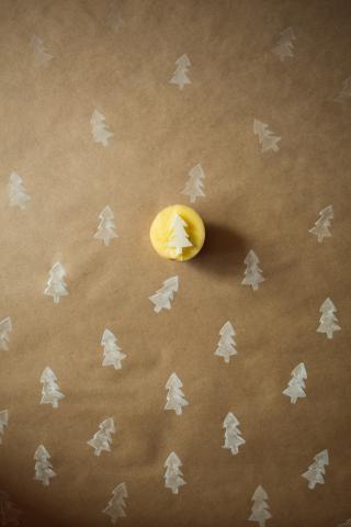 Brown kraft paper background with white pine trees stamped on top, featuring a carved potato with a pine tree. 