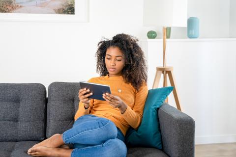 woman on couch reading on her tablet computer