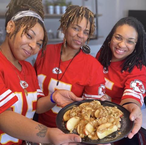 Stacey stands in the middle surrounded by her daughters and holding a baked apple dish. 