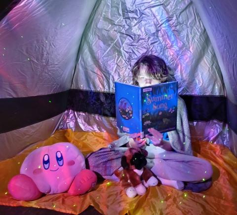 Student reading a book in a tent.