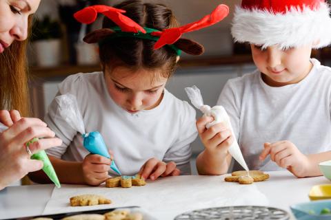 one adult and two children decorating cookies using icing in bags