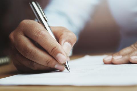 A hand holding a pen, writing on a notepad.