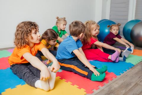 Children seated on colorful mats stretching to touch their toes