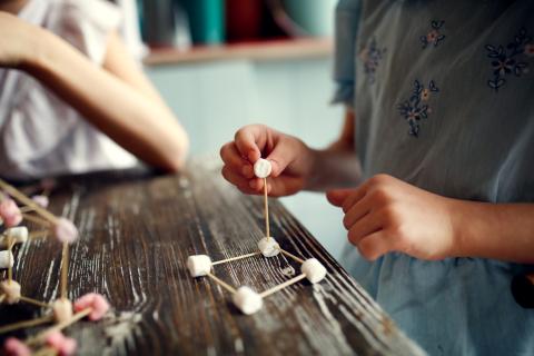 Hands building a structure with marshmallows and toothpicks