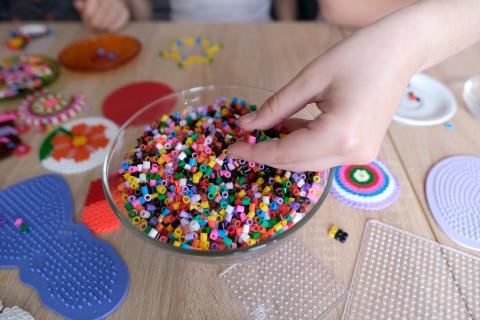 Adobe Stock Image of a child's hand in holding perler beads and a bowl full of perler beads