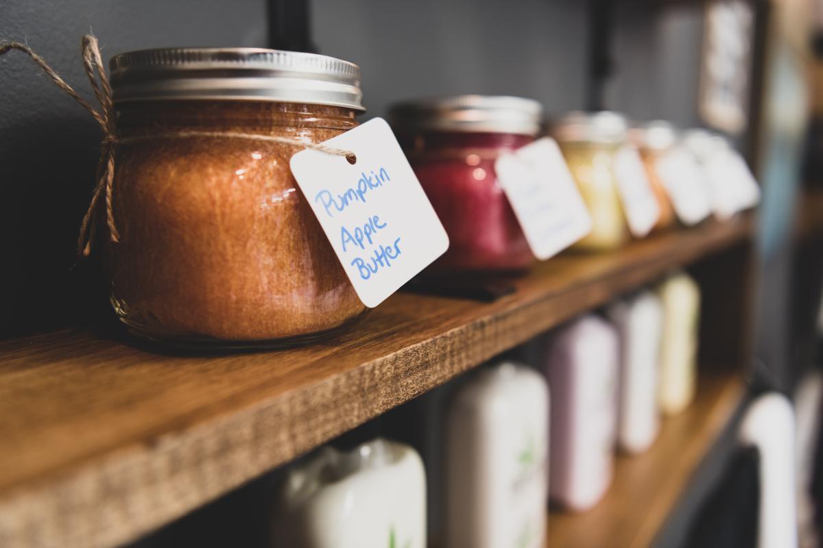 A shelf of country styled mason jars. The front jar is filled with pumpkin apple butter. 