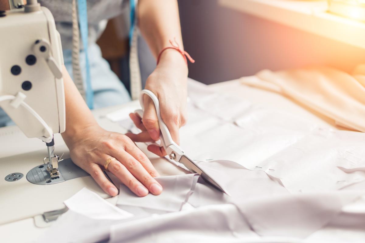 A woman's hands cutting fabric next to a sewing machine