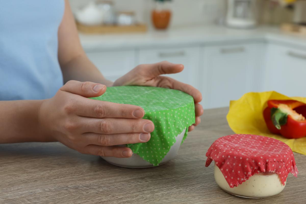 A pair of hands smoothing down the sides of a green bee's wax wrap onto a bowl. 