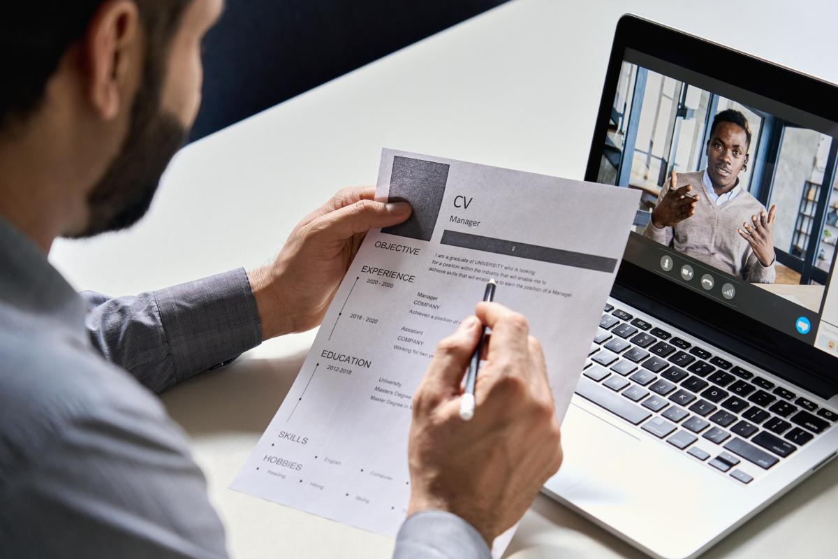 a man holding resume in his hand interviews another man virtually