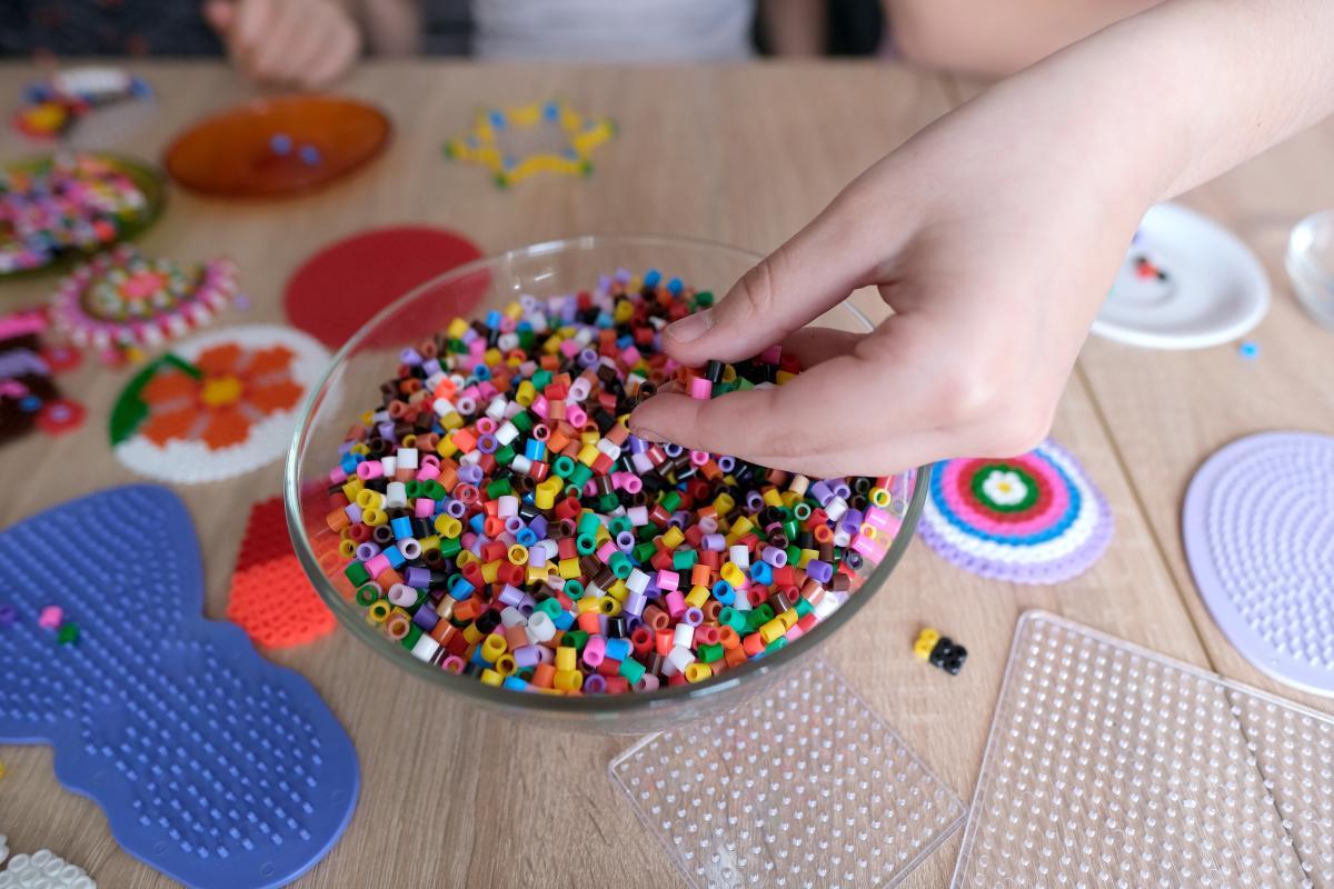 Adobe Stock Image of a child's hand in holding perler beads and a bowl full of perler beads